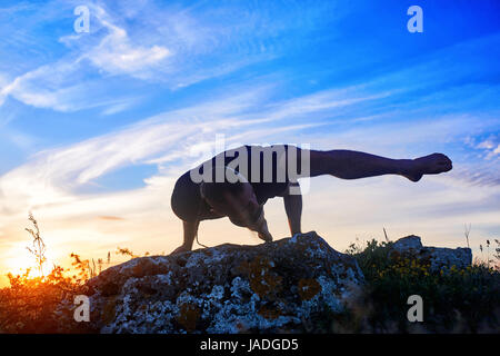 Attractive man doing yoga on the rock in the morning against sunrise. Stock Photo