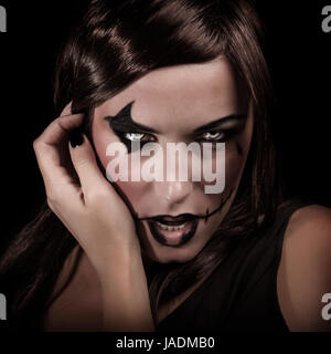 Scary portrait of young woman with aggressive makeup isolated on black background, terrifying witch, spooky vampire, Halloween party concept Stock Photo