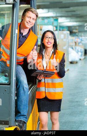 Logistics Teamwork - forklift driver, Worker or warehouseman and his coworker with tablet computer at warehouse of freight forwarding company Stock Photo