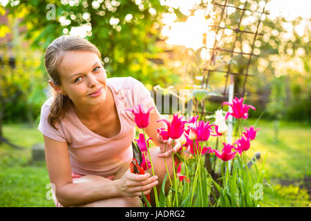 Pretty female gardener taking care of her lovely garden on a spring day - admiring the tulips Stock Photo
