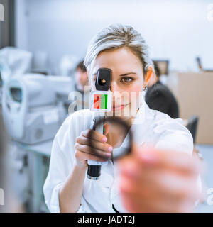 Optometry concept - pretty young optometrist at work, examinating your eyes (color toned image; shallow DOF) Stock Photo