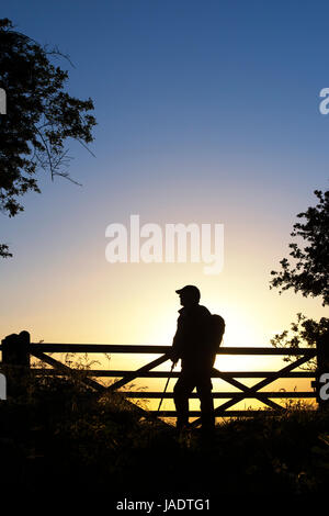 Silhouette walker standing by a gate along the cotswold way at sunset on Broadway hill. Cotswolds, Broadway, Gloucestershire, England Stock Photo