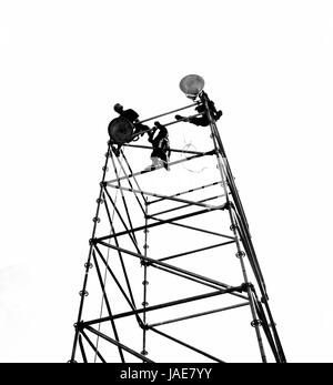 Workers set up powerful lights on scaffolds, seen in silhouette Stock Photo