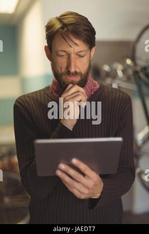 Thoughtful employee using digital tablet at bicycle workshop Stock Photo