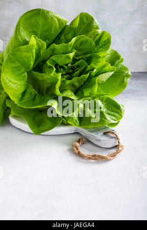 A single head of crisp green iceberg lettuce on a textured gray ...