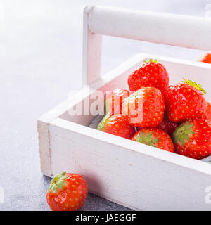 White wooden box filled with succulent juicy fresh ripe red strawberries on gray stone table top. Healthy food. Copy space. Stock Photo