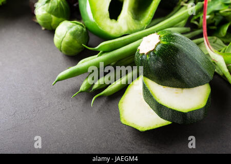 Fresh zucchini with assorted green vegetables, salad, peas and Brussels sprouts on brown stone table top. Healthy food concept with copy space. Stock Photo