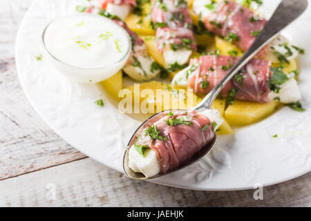 Rolls of mozzarella, basil and Parma ham on slices of mango with yoghurt sauce on white plate. Healthy eating concept. Stock Photo