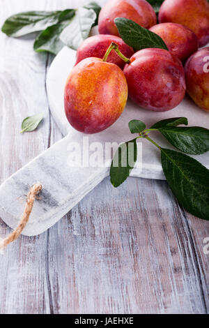 Fresh plums on marble cutting board on old white wooden background. Selective focus. Healthy food concept. Copy space. Stock Photo