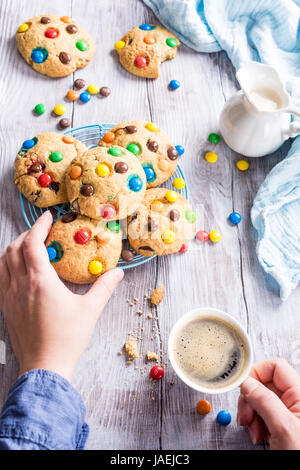 Homemade cookies with colorful chocolate candies with cup coffee on old white wooden table. Stock Photo