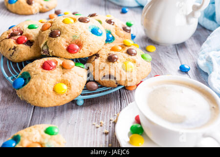 Homemade cookies with colorful chocolate candies with cup coffee on old white wooden table. Stock Photo