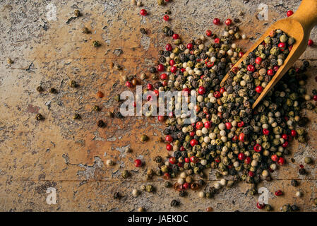 Multi-colored peppercorns in a wooden bucket on a old plank Stock Photo