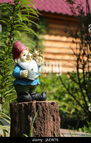 Little garden gnome figurine standing on a tree stump in the backyard Stock Photo