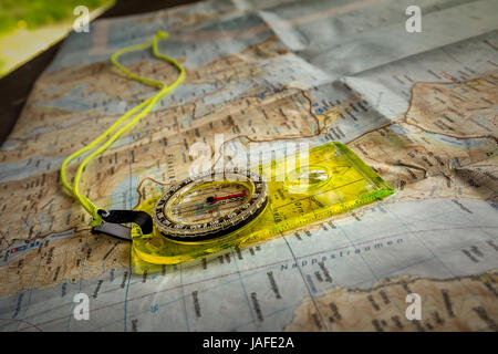 Finding position with yellow compass lying on tourist map on wooden table located in shed. Stock Photo