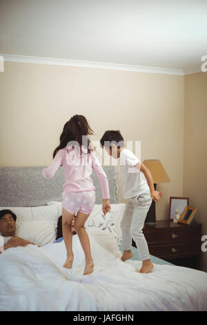 Siblings jumping on bed in bedroom at home Stock Photo