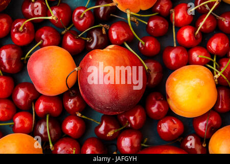 Ripe glossy sweet cherries with water drops, nectarines, apricots scattered on dark blue background, seamless pattern, template, vibrant colors, top v Stock Photo