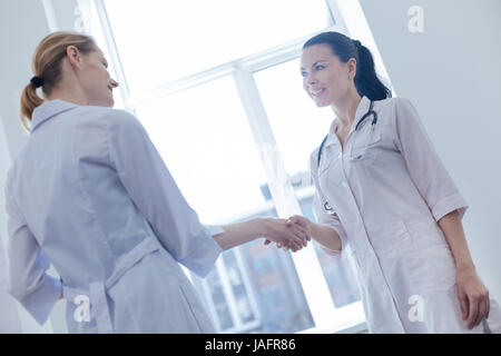 Nice to meet you. Smiling pleasant young nurses standing in the clinic and enjoying conversation while handshaking Stock Photo