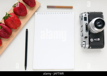 Notebook mock up for artwork with old camera, pen and red strawberries. Top view. Place for text Stock Photo