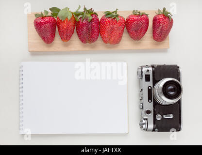 Notebook mock up for artwork with old camera, pen and red strawberries. Top view. Place for text Stock Photo