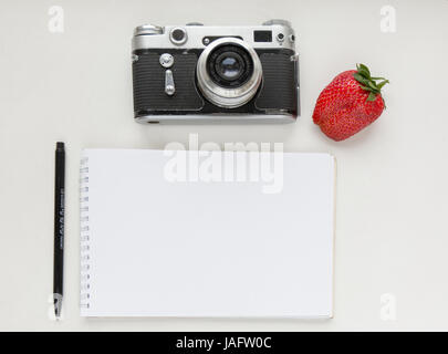 Notebook mock up for artwork with old camera, pen and red strawberries. Top view. Place for text Stock Photo
