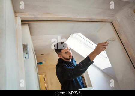 A builder, painter holding a paint brush, painting a door frame. Stock Photo