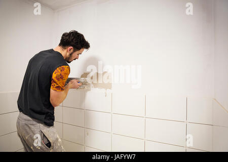 A builder, tiler placing white ceramic tiles on a wall in a bathroom. Stock Photo