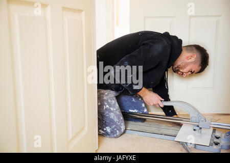 A builder, tiler kneeling on the floor, cutting a tile. Stock Photo