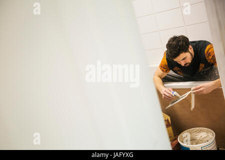 A builder, tiler working in a bathroom, spreading adhesive on a tile. Stock Photo