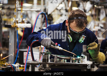 A man in a facemask with breathing filters, a skilled factory worker welding arts of a bicycle in a factory. Stock Photo