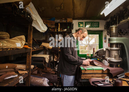 Man standing in a shoemaker's workshop, cutting brown leather. Stock Photo