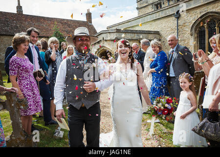 Smiling bride and groom leaving church, guest throwing confetti. Stock Photo