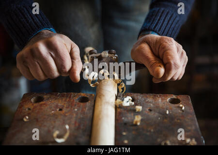 Man standing in a workshop, holding a plane, planing and shaving a piece of wood in a clamp. Stock Photo