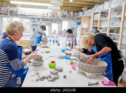 Five people, women in a pottery studio, working on handbuilding clay objects.