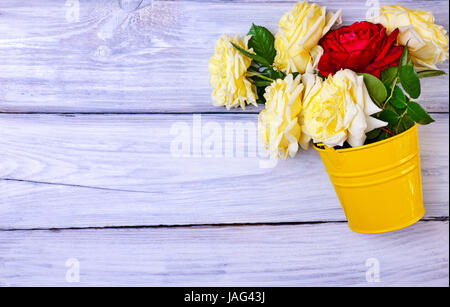 Bouquet of fresh roses in a yellow iron bucket on a white wooden background, empty space on the left Stock Photo