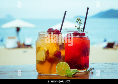 Close up of two glasses with refreshing strawberry cocktail with lime, apple and mint on sea beach background. Stock Photo