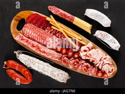 Assortment of different sliced meat snacks. Serving cold Italian appetizers On black natural stone from slate. On a wooden board from olive tree and w Stock Photo
