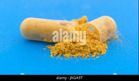Close view of turmeric capsule opened spilling the ground contents onto a blue background. Stock Photo