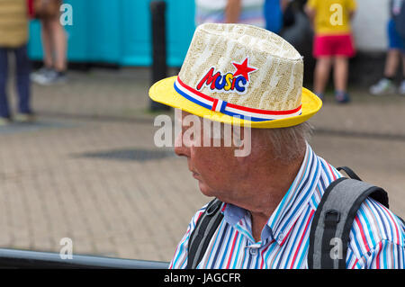 Man wearing striped shirt and hat with Music on at the Wessex Folk Festival at Weymouth, Dorset in June Stock Photo