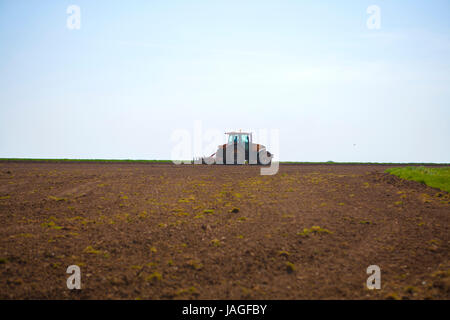 yellow tractor ploughing crops in field on clear blue sunny hot day Stock Photo