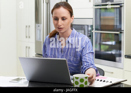 Female Freelance Worker Using Laptop In Kitchen At Home Stock Photo