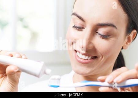Woman Squeezing Toothpaste Onto Tootbrush In Bathroom Stock Photo