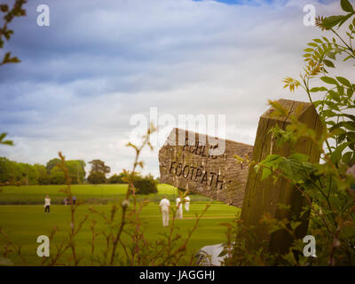 Public Footpath wooden sign with game of cricket being played in background Stock Photo