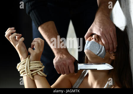 Terrified kidnapped woman being threatened by a kidnapper putting a knife in her neck indoors Stock Photo