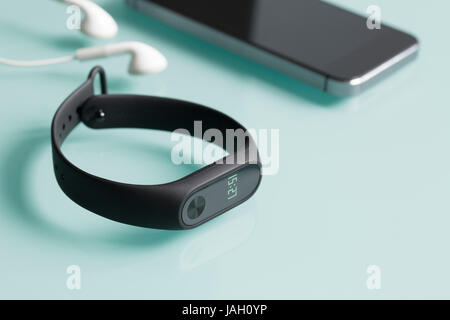 Fitness tracker, smartphone and earphones on green glass background. Stock Photo