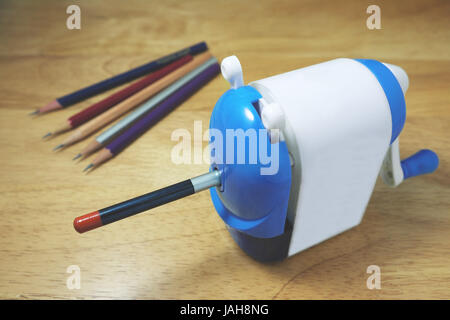 Pencil being sharpened in a pencil sharpener on wooden desk. Stock Photo