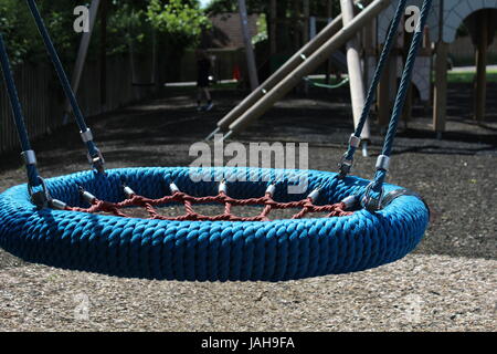 Close up of children's play equipment in a local park: dish swing with slide in background Stock Photo