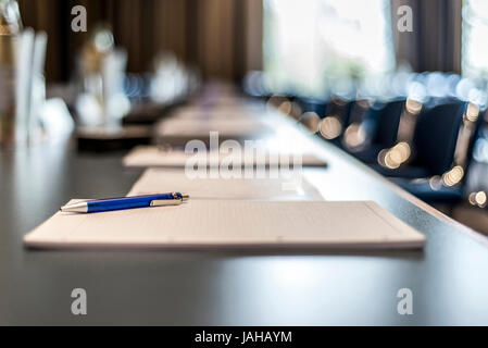 Close up of dark conference table with water glasses, pens, paper sheets and blurry window background Stock Photo
