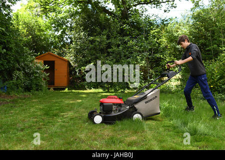 A young Boy cuts the grass in the garden as part of his chores for pocket money Stock Photo
