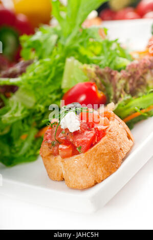 original Italian fresh bruschetta,typical finger food, with fresh salad and vegetables on background Stock Photo