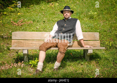 Man with traditional Bavarian costume is sitting on a bench Stock Photo